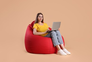 Beautiful young woman using laptop on red bean bag chair against beige background