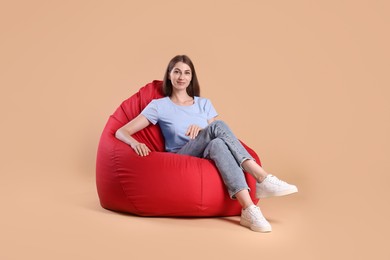 Photo of Beautiful young woman sitting on red bean bag chair against beige background