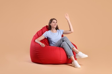 Smiling woman sitting on red bean bag chair against beige background