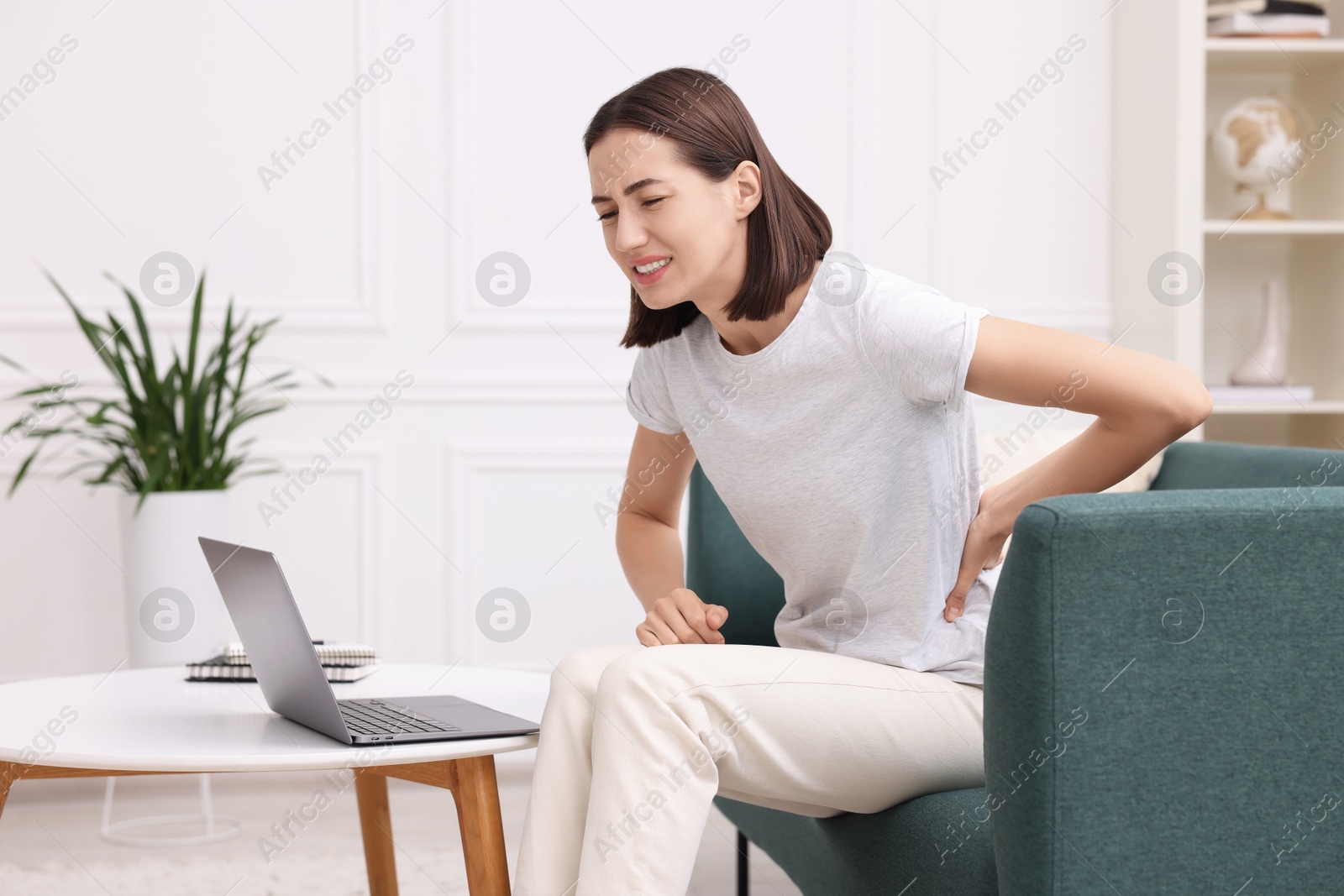 Photo of Woman suffering from back pain at home. Symptom of poor posture