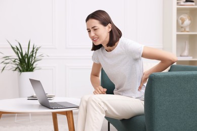 Photo of Woman suffering from back pain at home. Symptom of poor posture