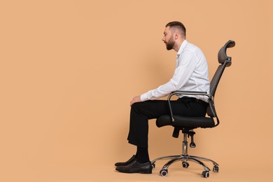 Man with poor posture sitting on chair against pale orange background, space for text