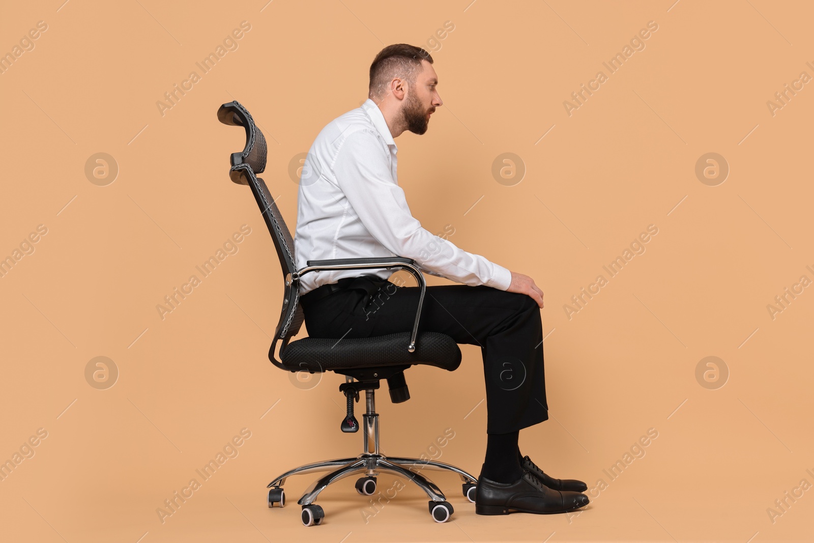 Photo of Man with poor posture sitting on chair against pale orange background