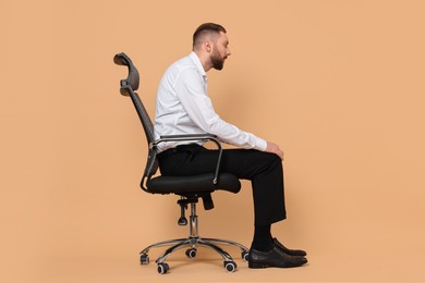 Photo of Man with poor posture sitting on chair against pale orange background