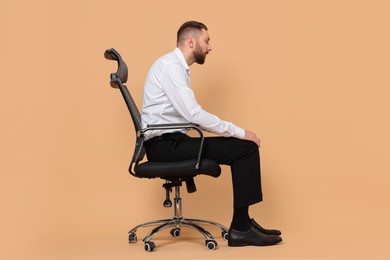 Man with poor posture sitting on chair against pale orange background