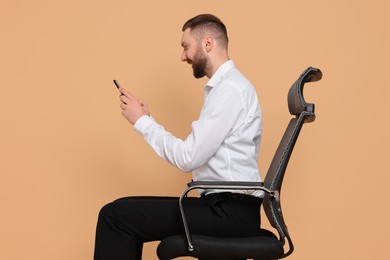 Man with good posture sitting on chair and using smartphone against pale orange background