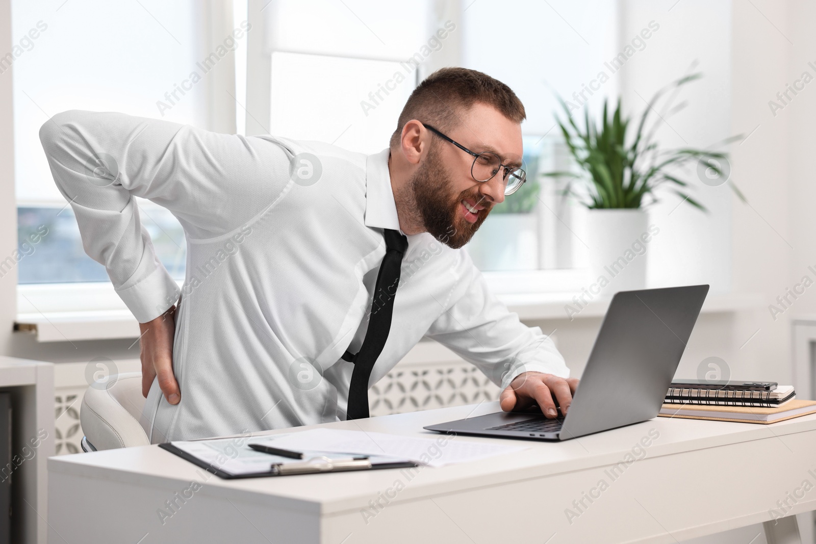 Photo of Man suffering from back pain in office. Symptom of poor posture