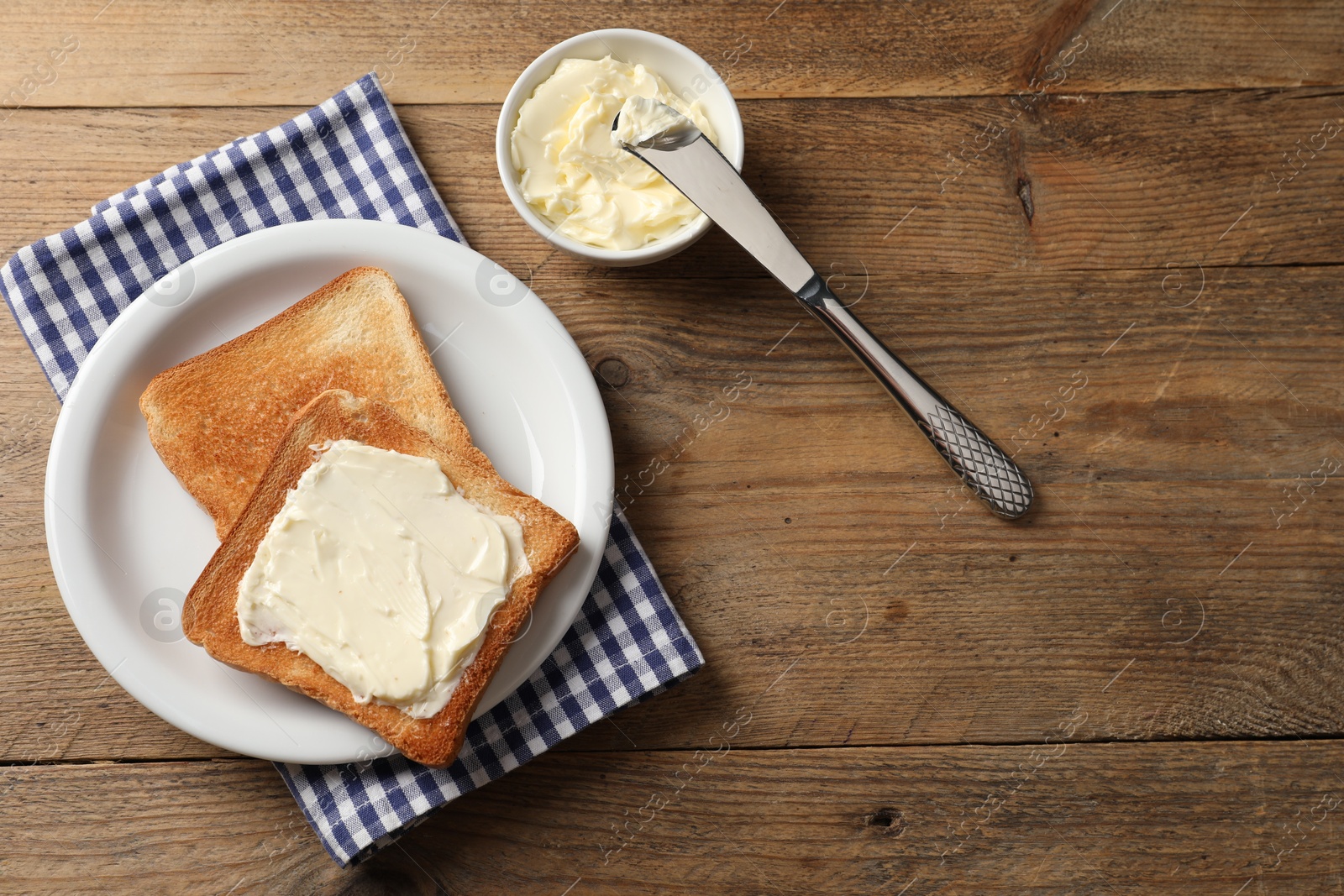 Photo of Delicious toasted bread slices with butter and knife on wooden table, flat lay