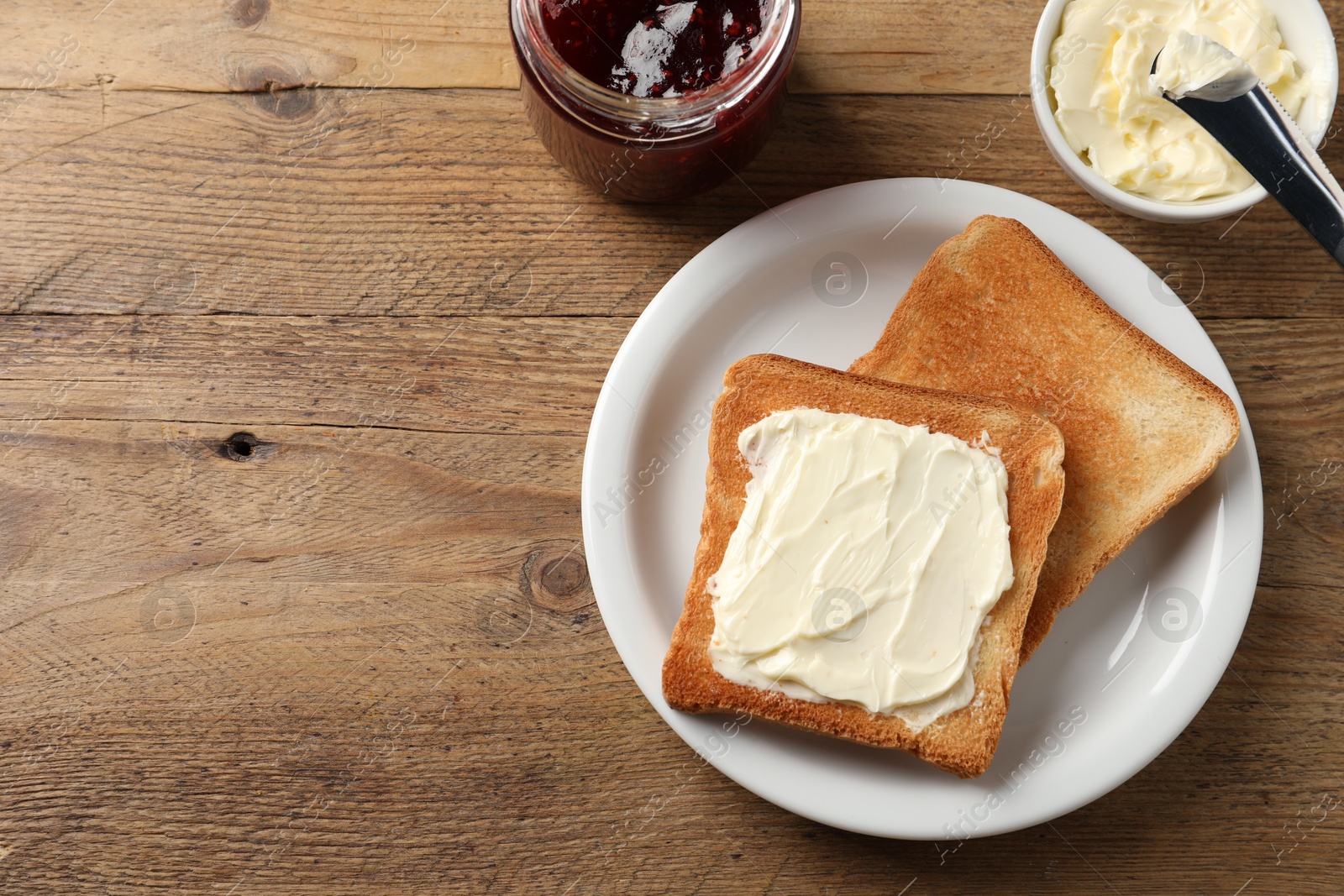 Photo of Delicious toasted bread slices with butter served on wooden table, flat lay. Space for text