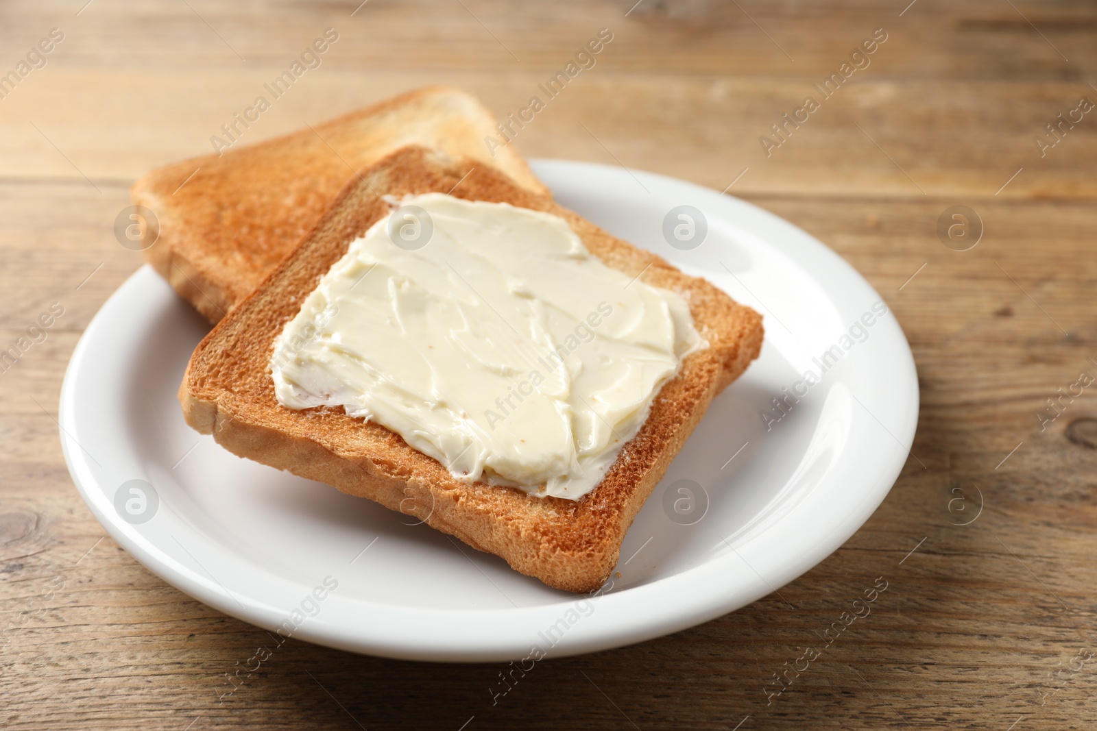 Photo of Delicious toasted bread slices with butter on wooden table, closeup