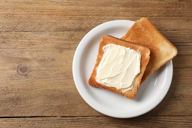 Photo of Delicious toasted bread slices with butter on wooden table, top view. Space for text