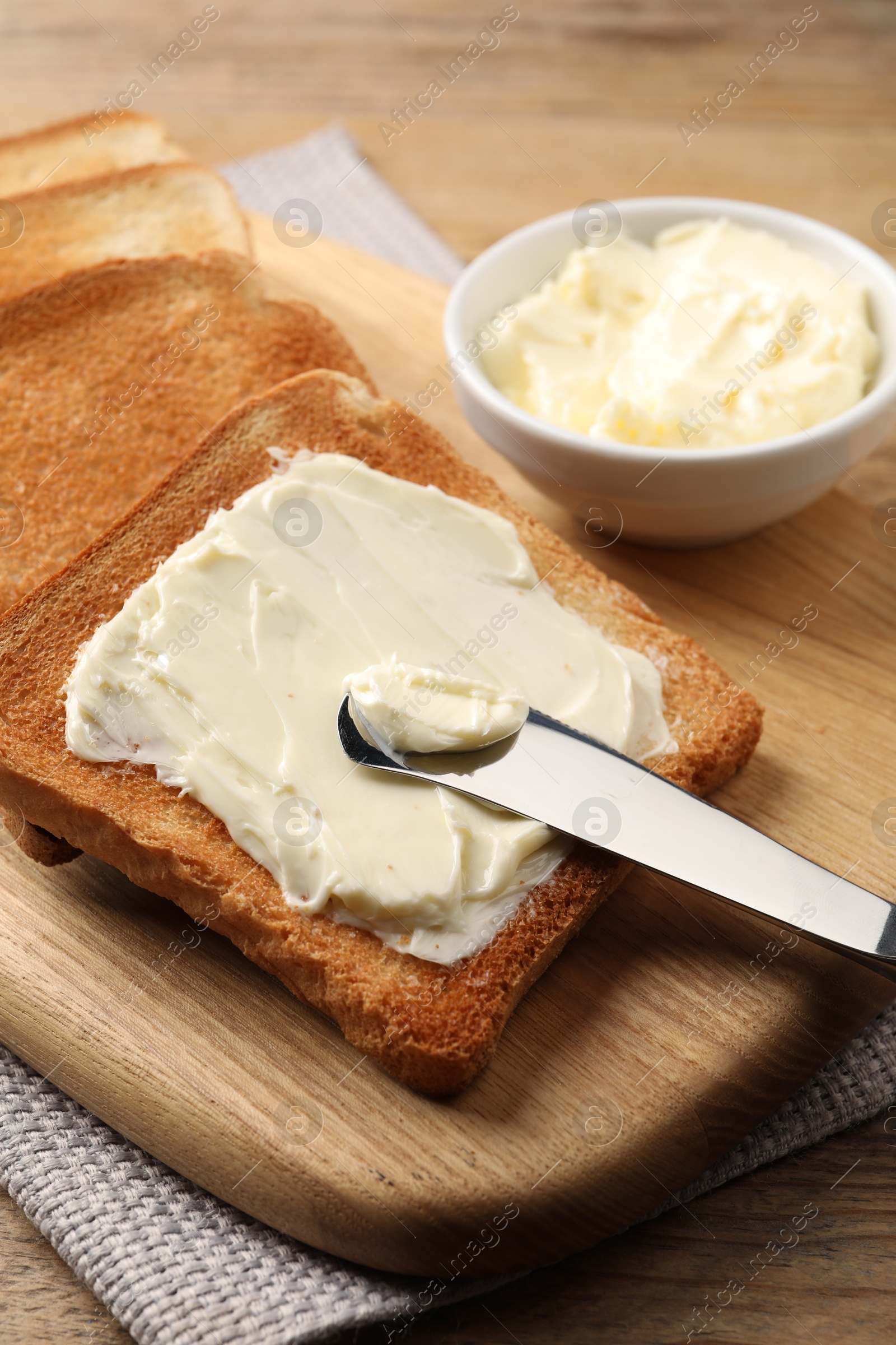 Photo of Delicious toasted bread slices with butter and knife on wooden table, closeup