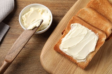 Delicious toasted bread slices with butter and knife on wooden table, flat lay