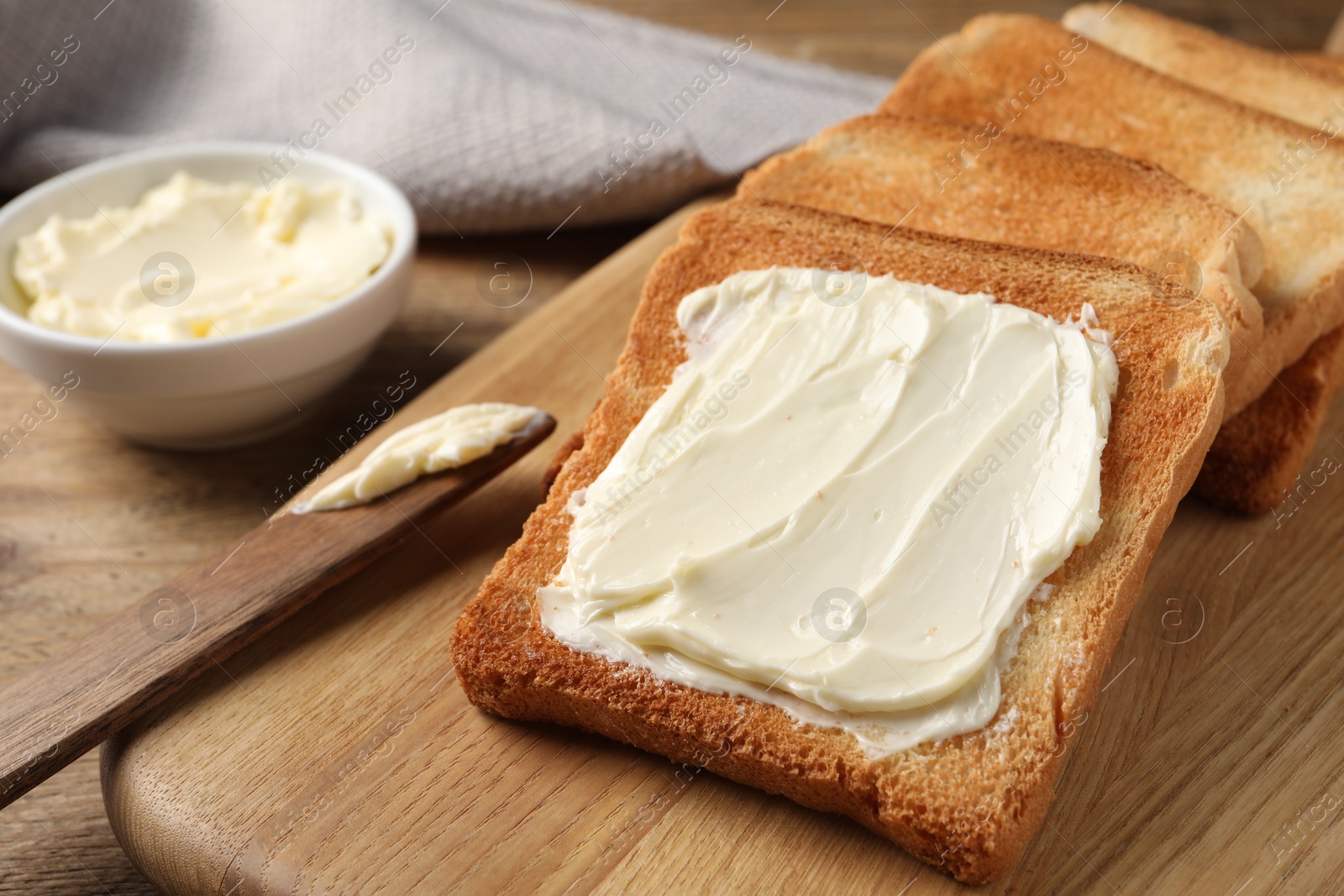 Photo of Delicious toasted bread slices with butter and knife on wooden table, closeup