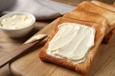 Photo of Delicious toasted bread slices with butter and knife on wooden table, closeup