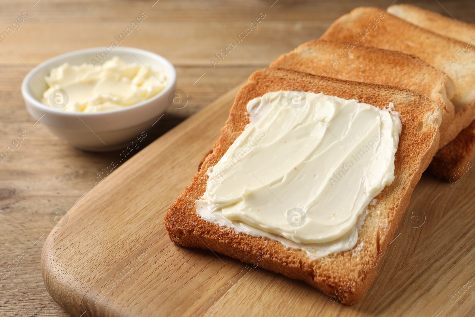 Photo of Delicious toasted bread slices with butter on wooden table, closeup