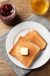 Photo of Delicious toasted bread slices with butter served on wooden table, flat lay