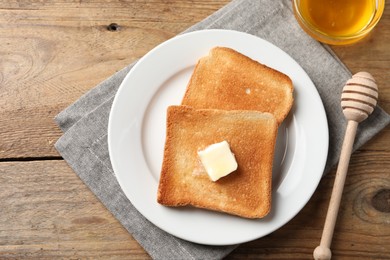 Delicious toasted bread slices with butter and honey on wooden table, flat lay