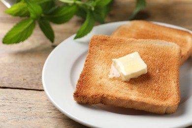 Photo of Delicious toasted bread slices with butter on wooden table, closeup