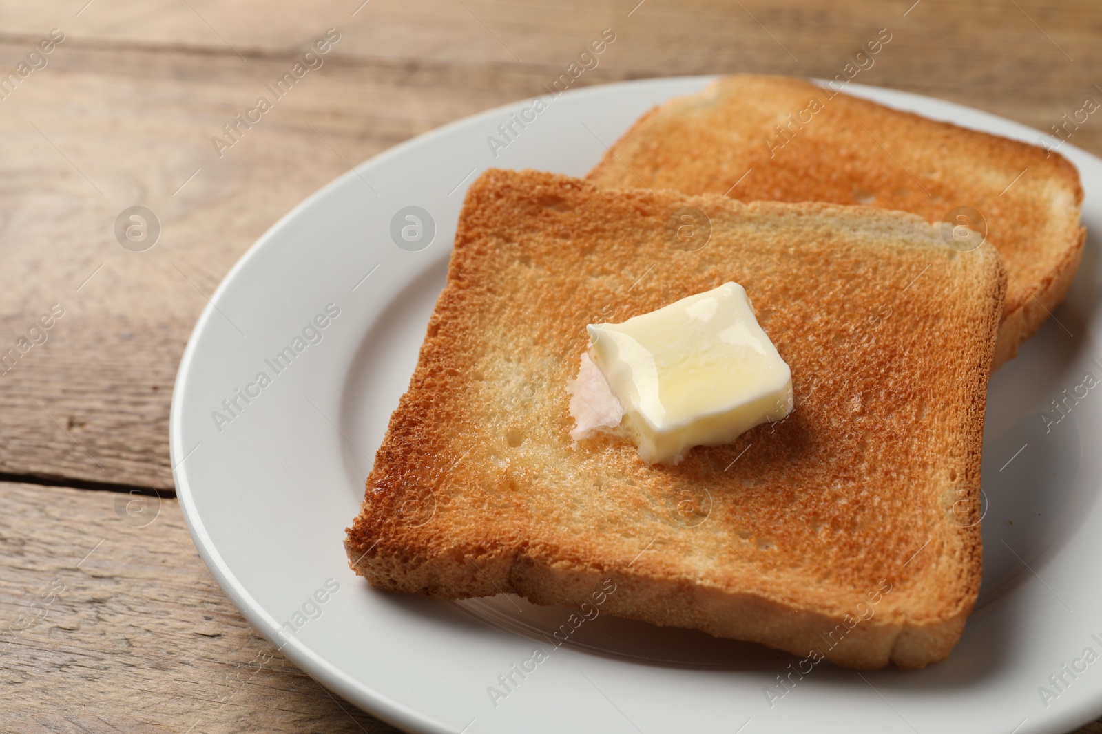 Photo of Delicious toasted bread slices with butter on wooden table, closeup