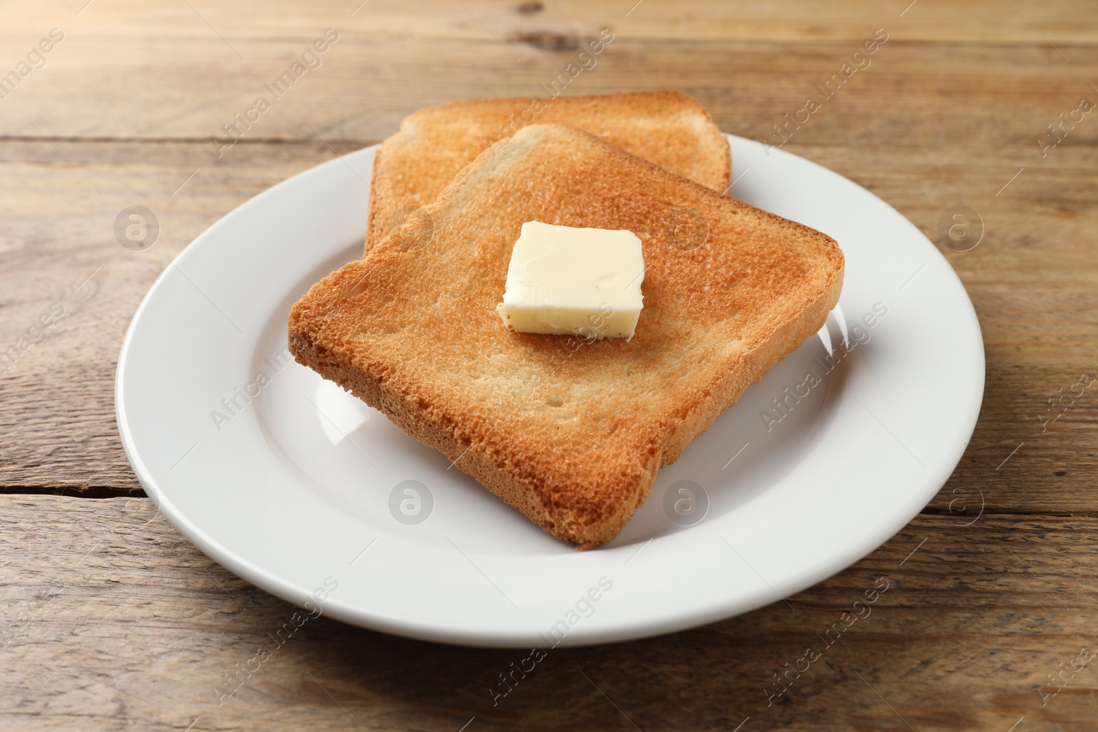 Photo of Delicious toasted bread slices with butter on wooden table