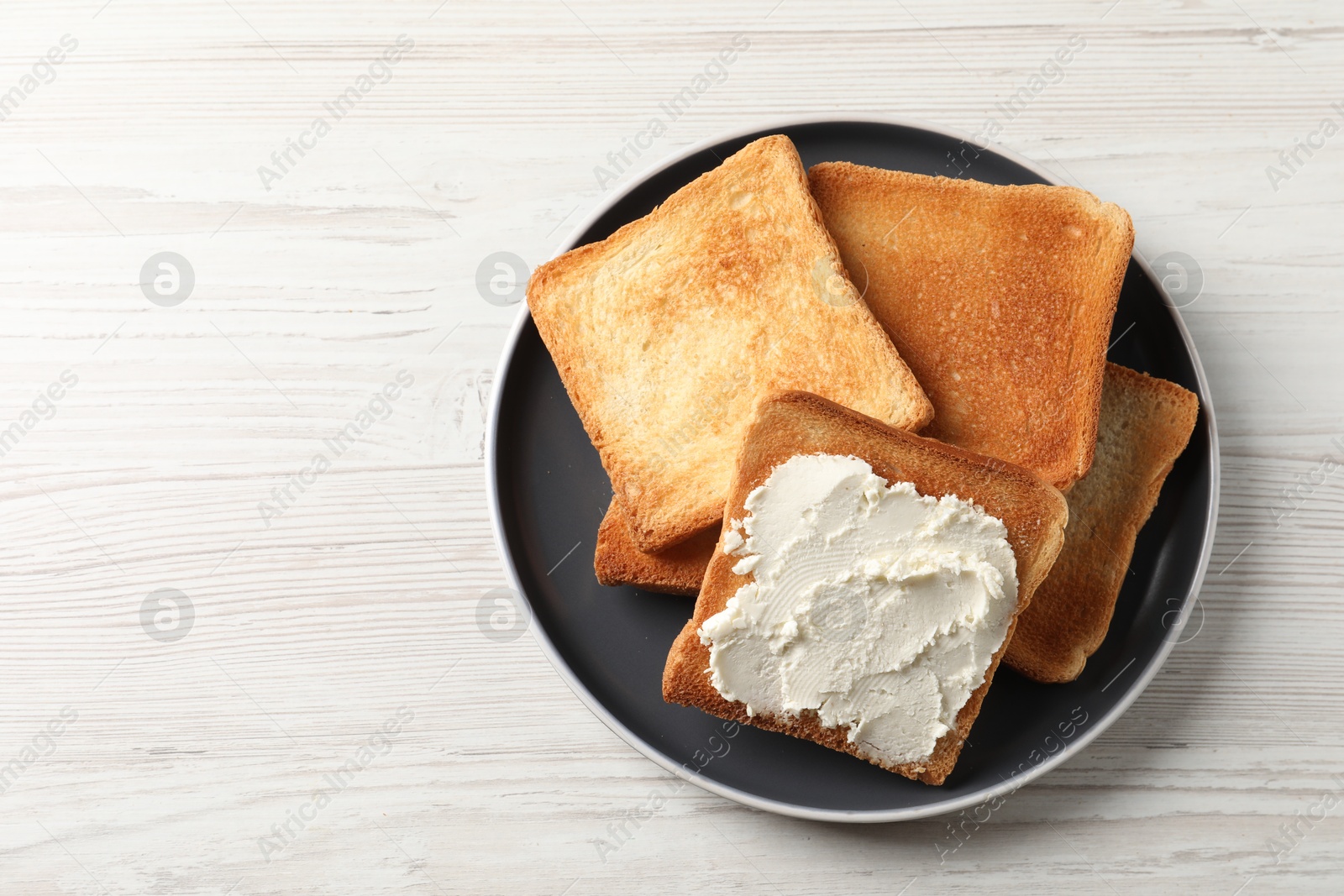 Photo of Delicious toasted bread slices with cream cheese on white wooden table, top view. Space for text