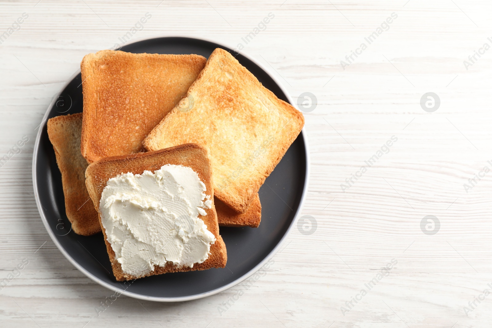 Photo of Delicious toasted bread slices with cream cheese on white wooden table, top view. Space for text