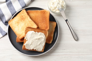 Delicious toasted bread slices with cream cheese and knife on white wooden table, flat lay