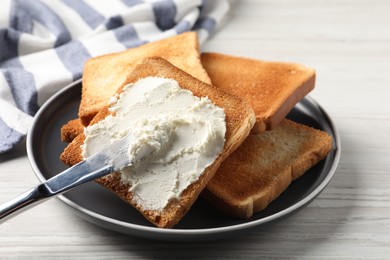 Delicious toasted bread slices with cream cheese and knife on white wooden table