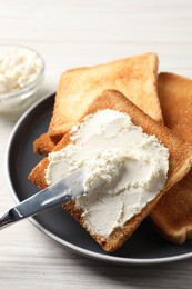 Delicious toasted bread slices with cream cheese and knife on white wooden table