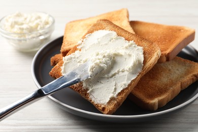 Delicious toasted bread slices with cream cheese and knife on white wooden table