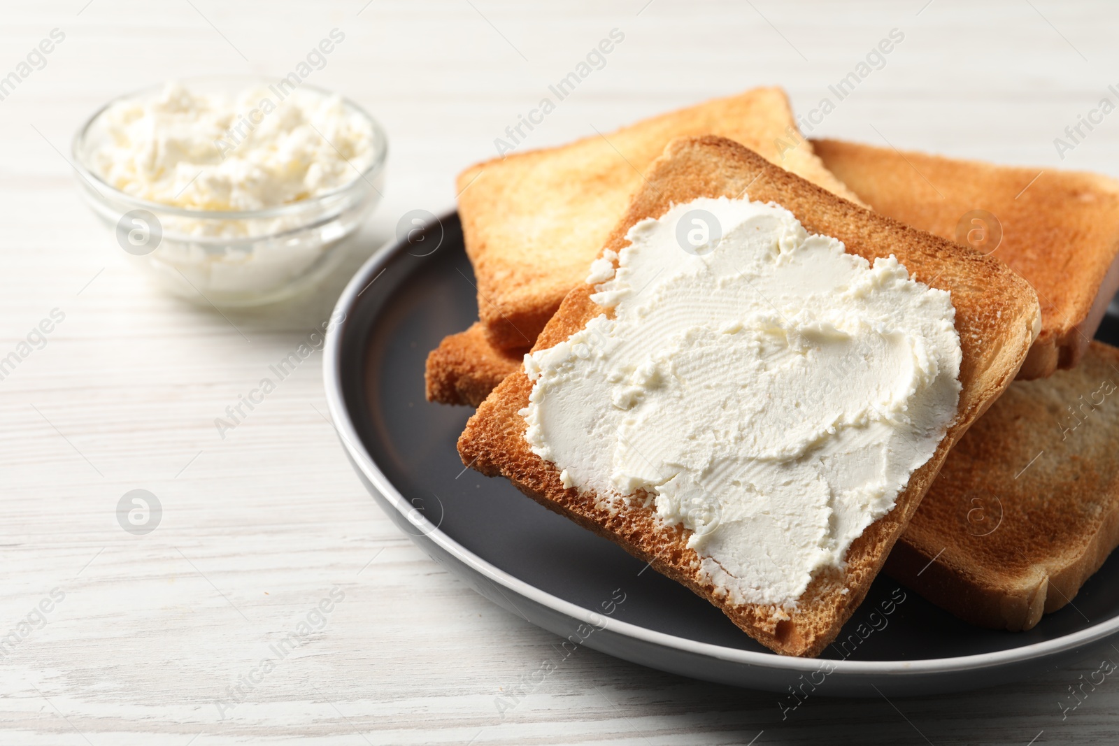 Photo of Delicious toasted bread slices with cream cheese on white wooden table