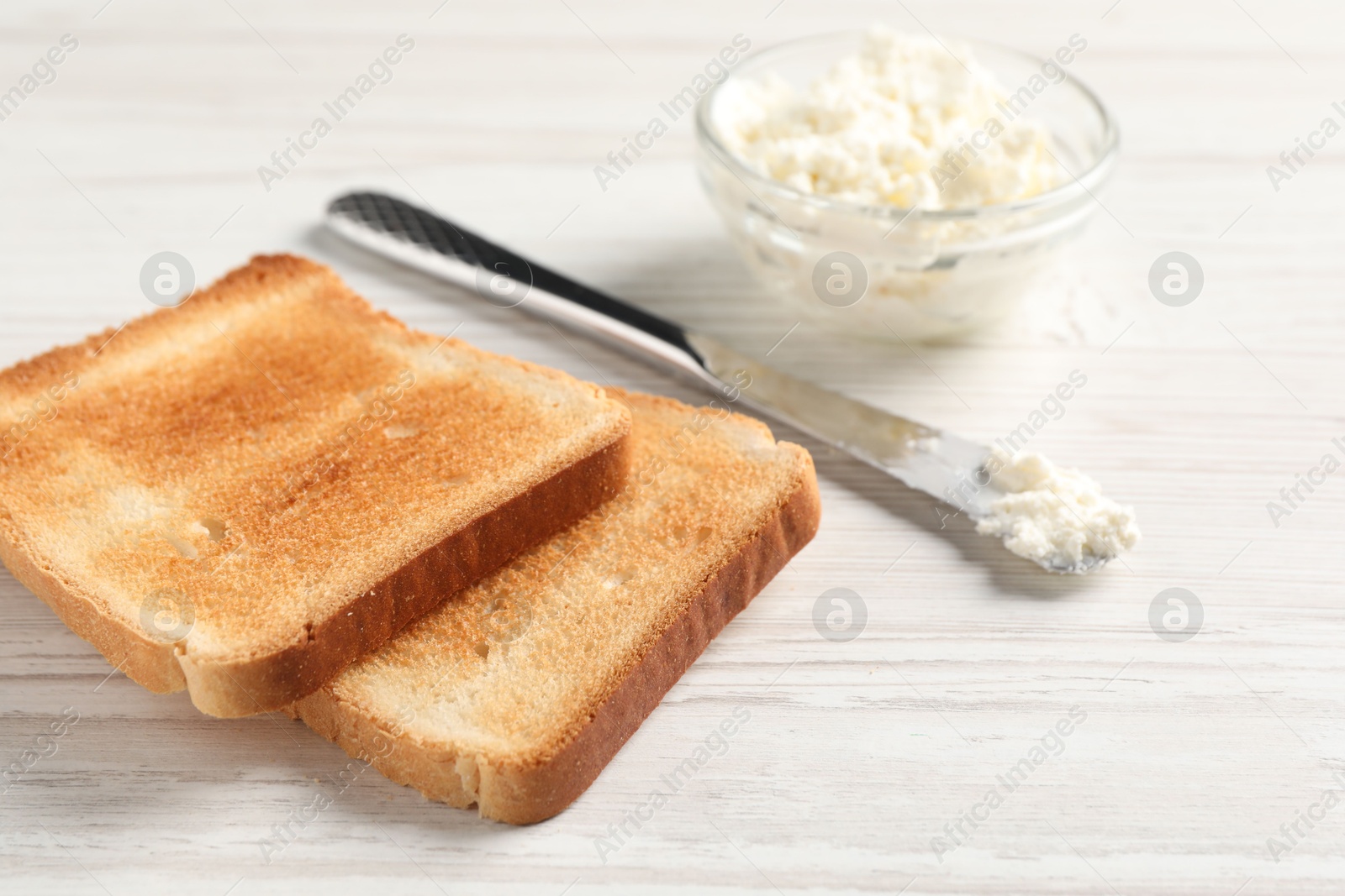 Photo of Delicious toasted bread slices with cream cheese and knife on white wooden table