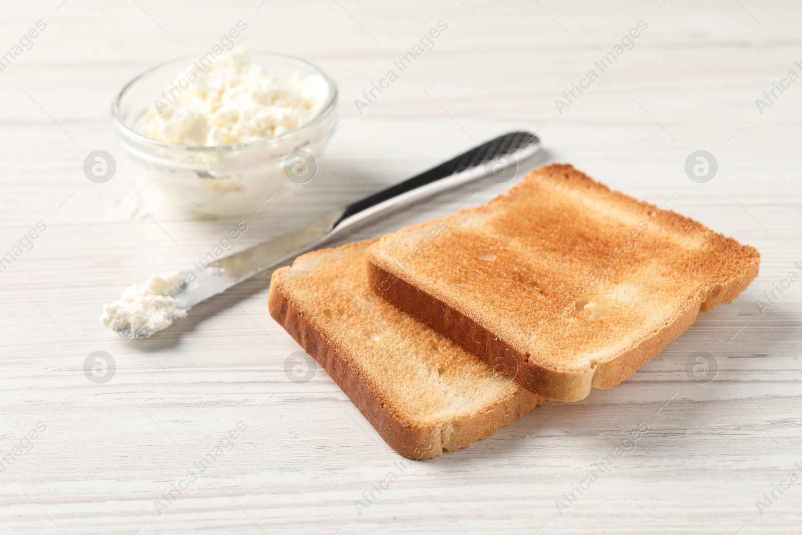 Photo of Delicious toasted bread slices with cream cheese and knife on white wooden table