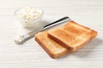 Delicious toasted bread slices with cream cheese and knife on white wooden table