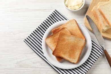 Delicious toasted bread slices with butter and knife on white wooden table, flat lay