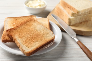 Delicious toasted bread slices with knife on white wooden table, closeup