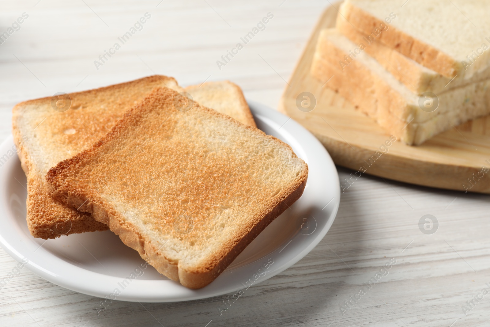 Photo of Delicious toasted bread slices on white wooden table, closeup