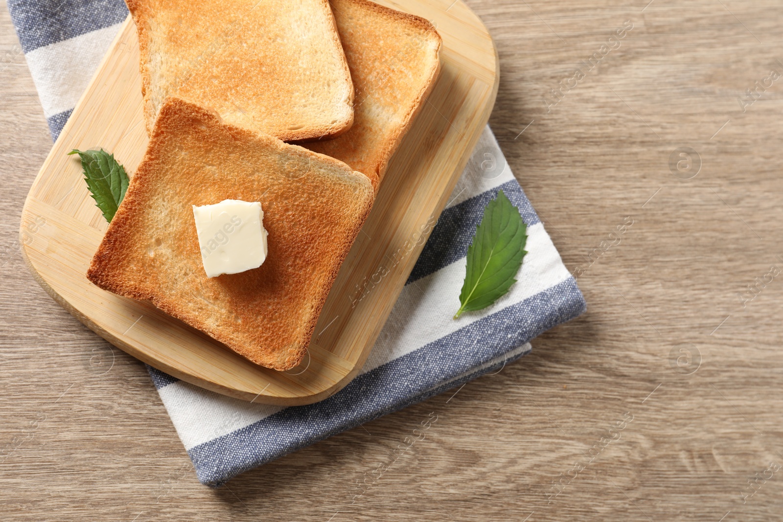 Photo of Delicious toasted bread slices with butter and mint on wooden table, top view. Space for text