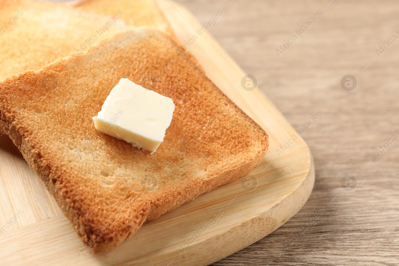 Photo of Delicious toasted bread slices with butter on wooden table, closeup