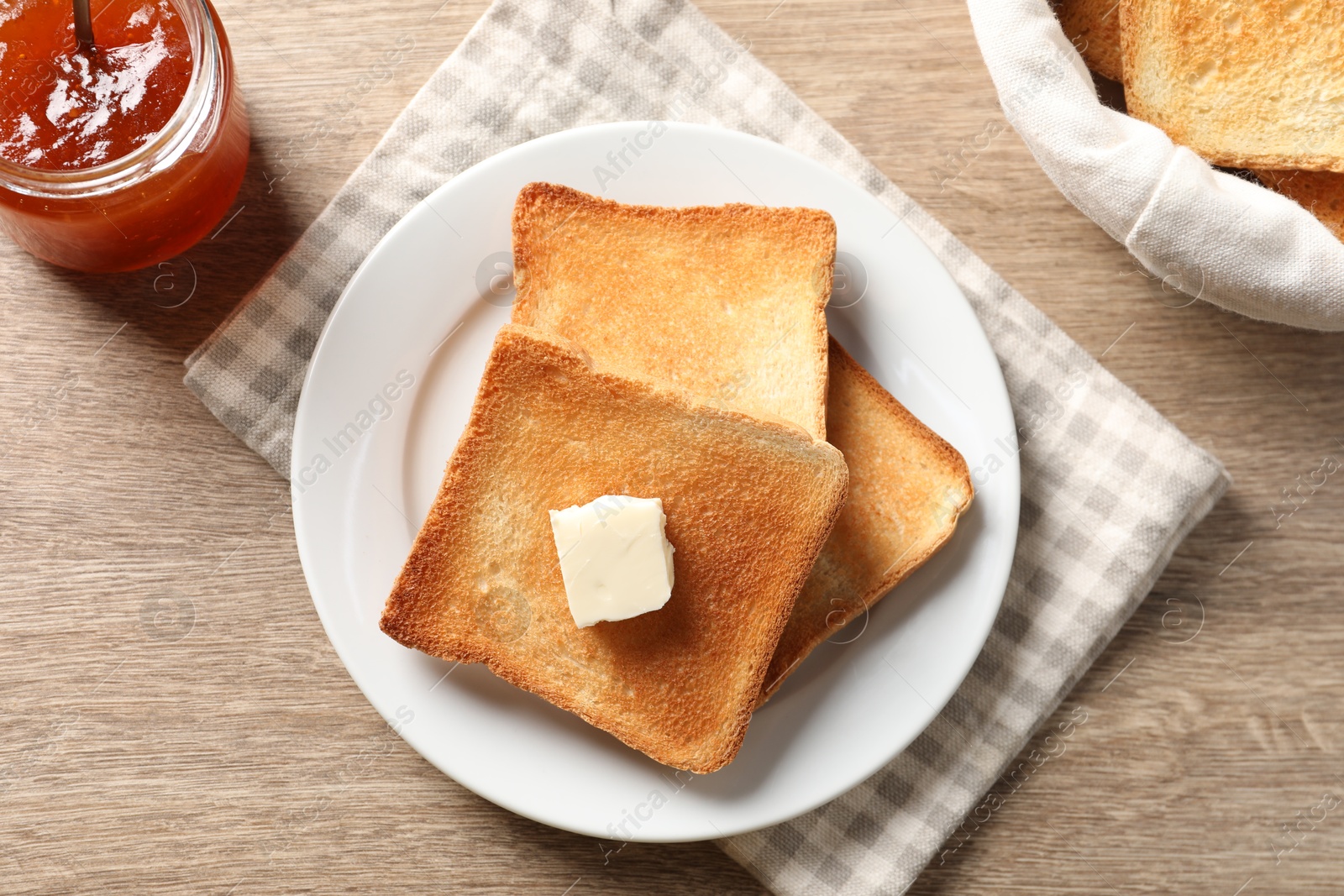 Photo of Delicious toasted bread slices with butter and jam on wooden table, flat lay