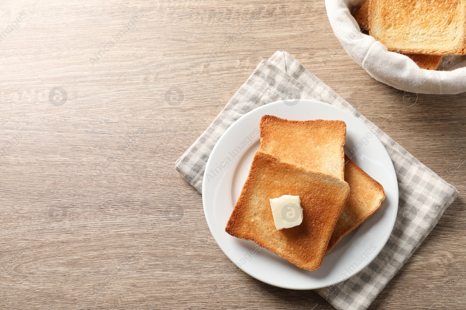 Photo of Delicious toasted bread slices with butter on wooden table, flat lay. Space for text