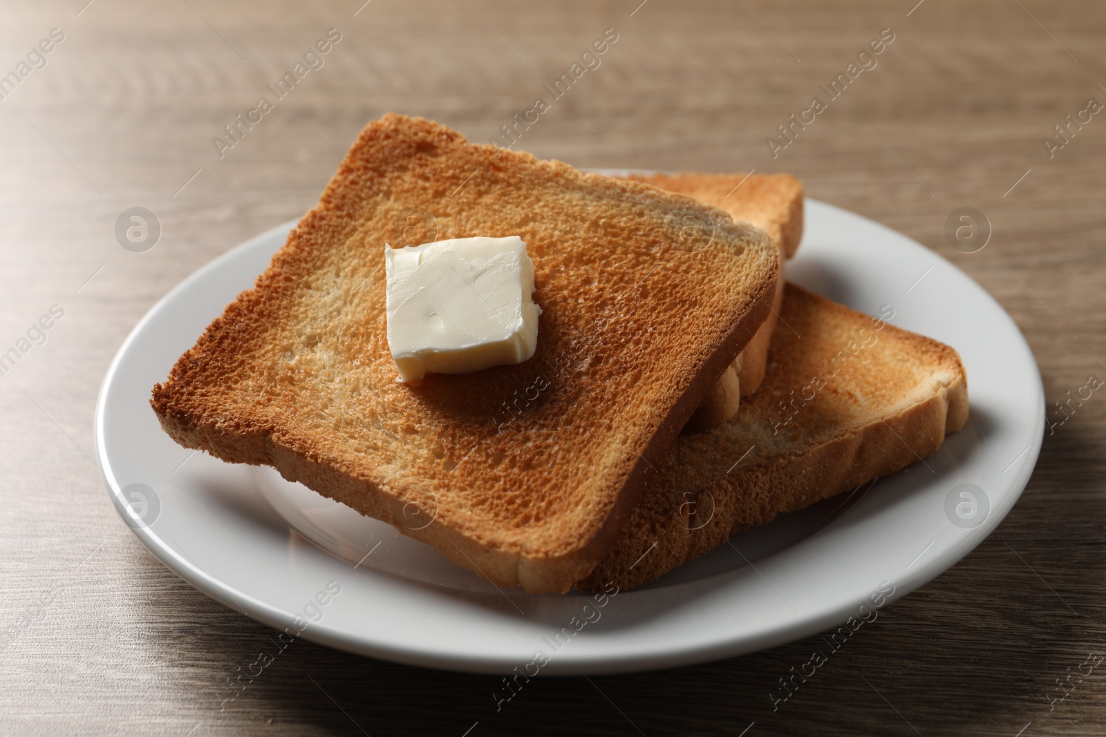 Photo of Delicious toasted bread slices with butter on wooden table, closeup