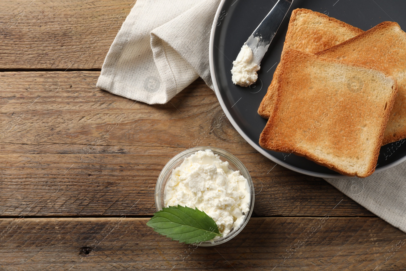 Photo of Delicious toasted bread slices with cream cheese, mint and knife on wooden table, flat lay