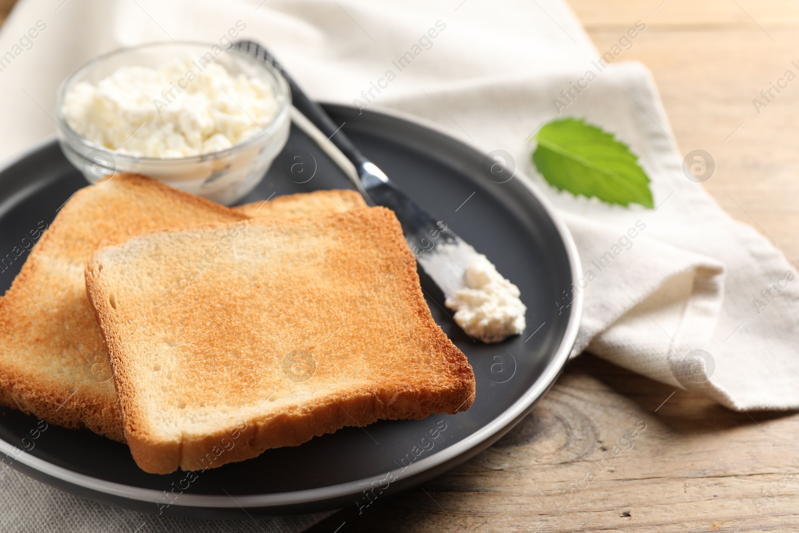 Photo of Delicious toasted bread slices with cream cheese and knife on wooden table, closeup