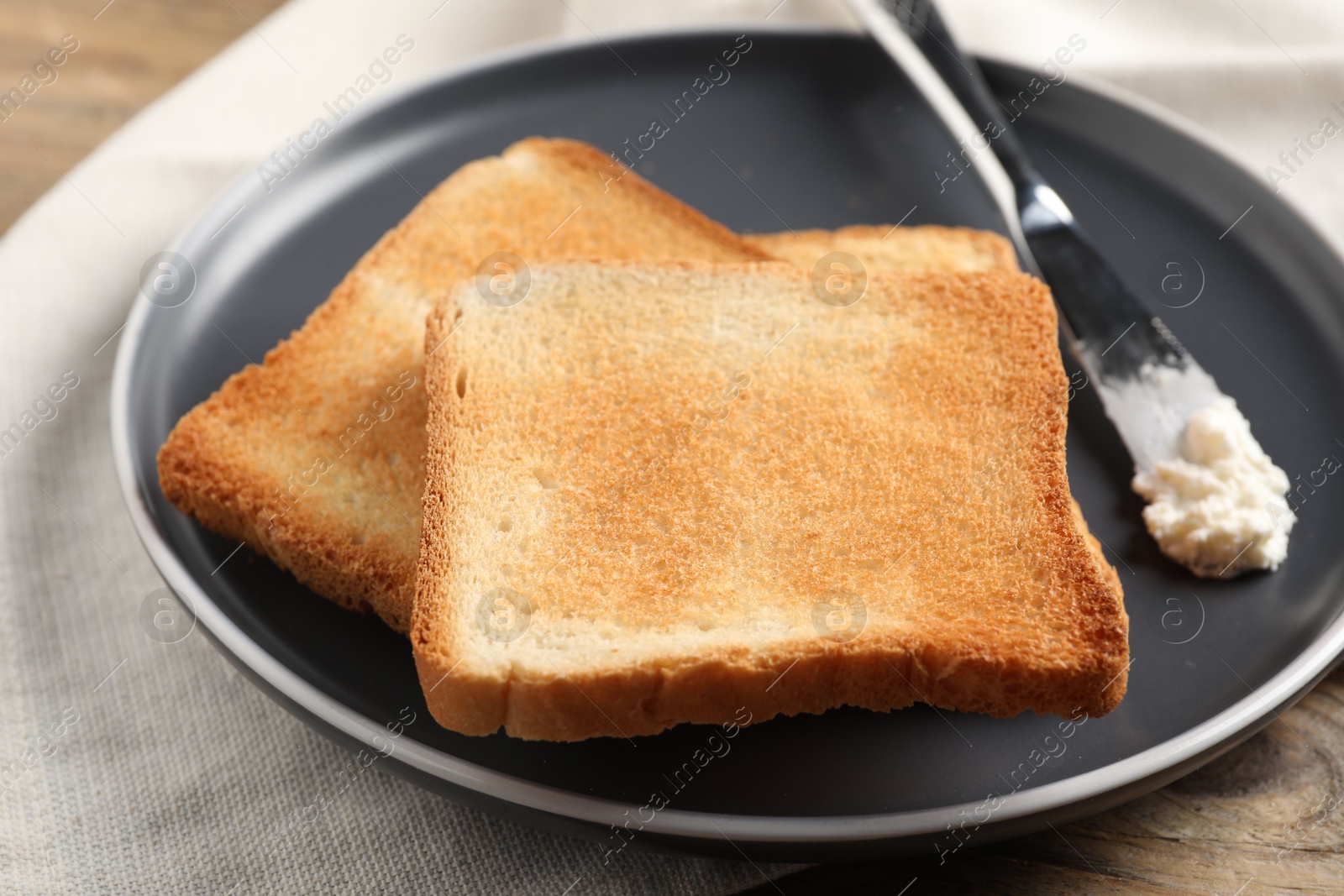 Photo of Delicious toasted bread slices with cream cheese and knife on table, closeup