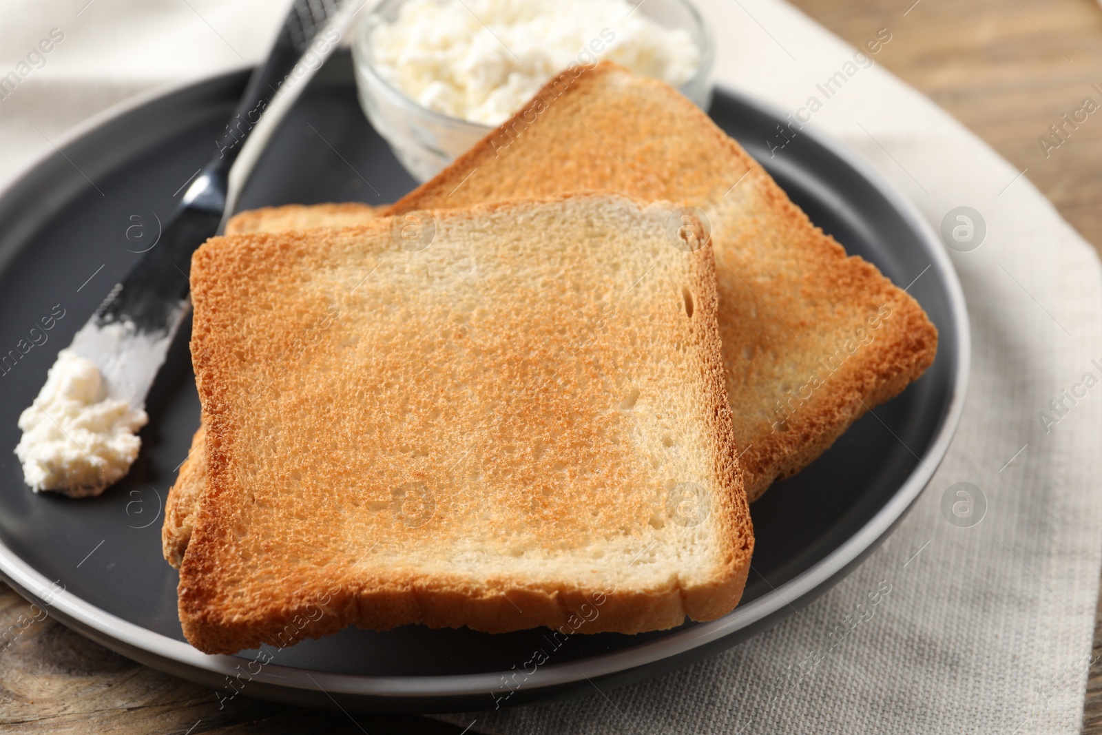 Photo of Delicious toasted bread slices with cream cheese and knife on table, closeup