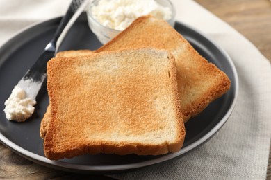 Photo of Delicious toasted bread slices with cream cheese and knife on table, closeup