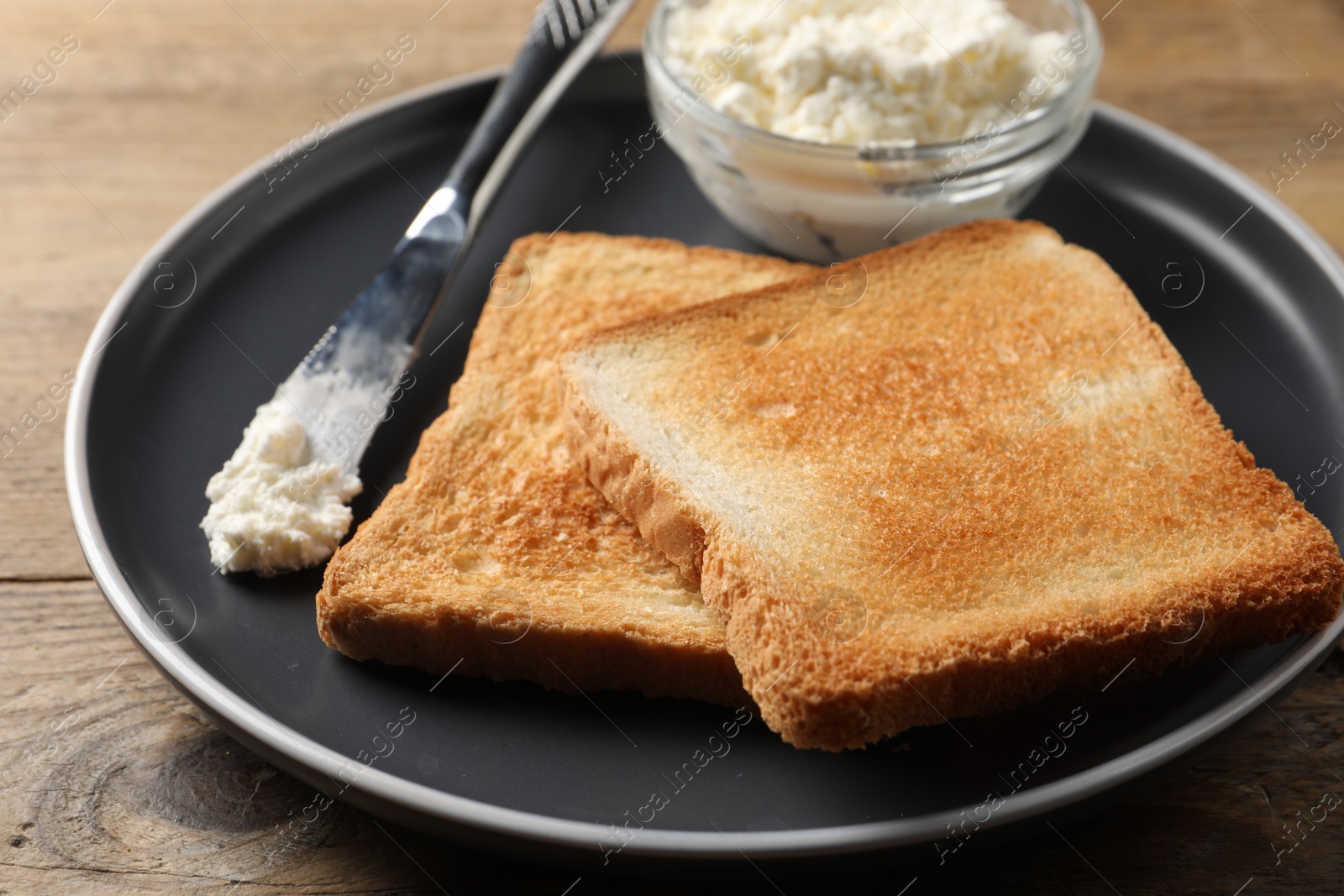 Photo of Delicious toasted bread slices with cream cheese and knife on wooden table, closeup