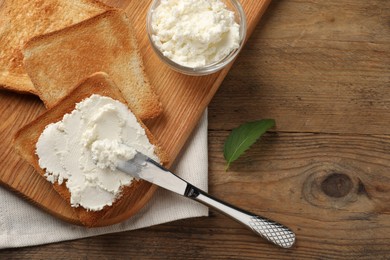 Photo of Delicious toasted bread slices with cream cheese, mint and knife on wooden table, flat lay